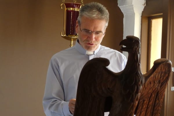 A minister in a clerical collar reading from an eagle lectern