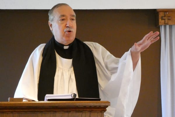 A minister in a white surplice and black stole preaching from the pulpit