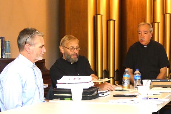 Three men seated at a table during a synod session